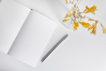 open white notebook with a pen on a white background with flowers. gentle composition of work, manuscript and study.