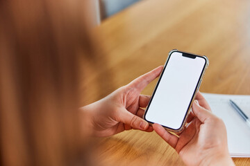 A close-up of a brunette holding a mobile phone with a blank white screen.