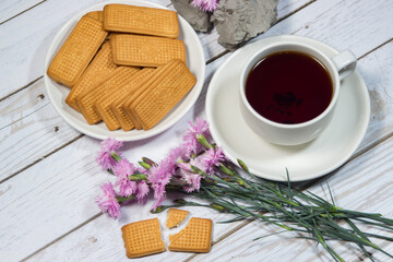 A cup of tea with cookies and flowers on a light table. Romantic breakfast