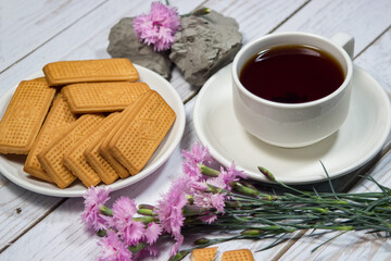 Fototapeta na wymiar A cup of tea with cookies and flowers on a light table. Romantic breakfast