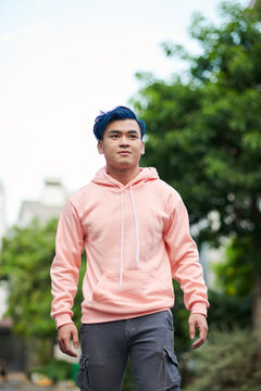 Positive teenage boy in salmon color hoodie walking in the street on summer day