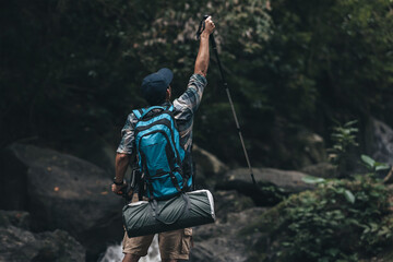 Hikers standing on the rock and raising hands to happy  with backpacks and background waterfall in the forest. hiking and adventure concept.