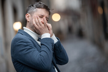 An adult man in blue jacket plays the harmonica on the street