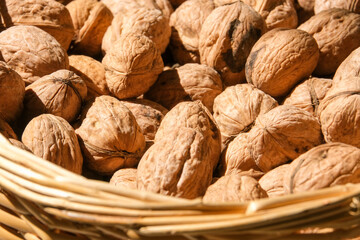 Close up organic whole unopened walnut shells inside wicker basket under sun. Unopened walnut shell background. Studio shot of unopened walnut. Selective focus area.