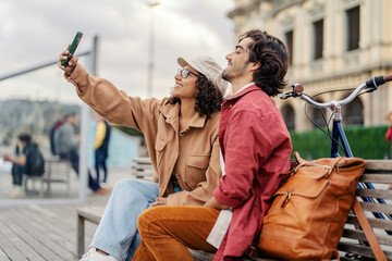 Naklejka premium Tourists are taking selfies while sitting on a bench on the city pier during their vacation in Spain.