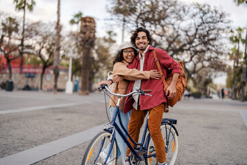 A happy romantic tourists with bike are hugging on a city street in Spain and smiling at the camera.