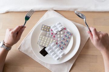 A handful of pills, capsules and colorful tablets on a plate near cutlery in female hands. Taking medication. Tablets instead of food. Concept of vitamins instead of food