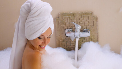 Sensual happy woman blowing foam in slow motion while playing with bubbles in a bathtub at an outdoor spa. The bottom view captures the beauty of her carefree moment of relaxation and happiness.