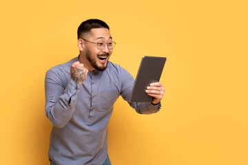 Online Success. Cheerful Asian Man With Digital Tablet Celebrating Win