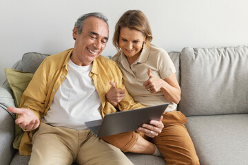 Smiling senior caucasian couple having video call via laptop with family, woman showing thumbs up to webcam