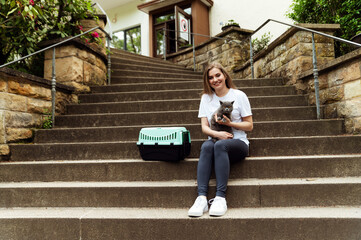 a cute girl holds a gray cat in her arms while being outside in nature. girl with a cat and a...