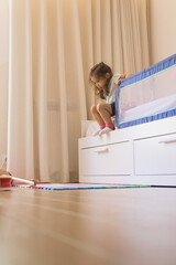 Small Caucasian girl playing in her bedroom, developing fine motor skills by getting on and off the...
