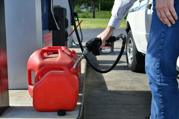 Man pumping gas from a gasoline pump into gas cans to transport it to another location.