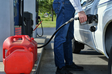Man pumping gasoline into a truck with gas cans ready for filling. 