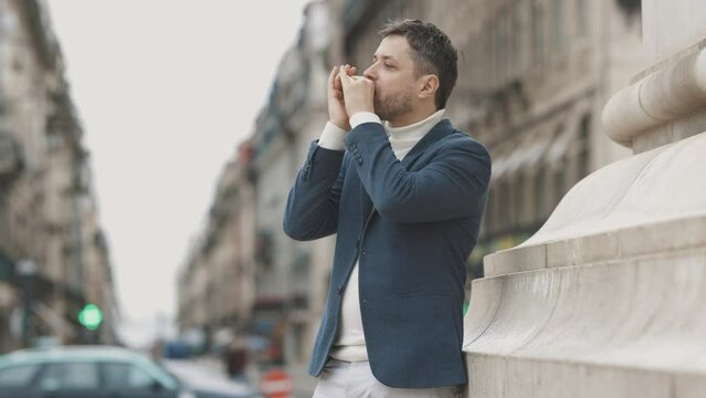 A man in a blue jacket plays the harmonica on the street