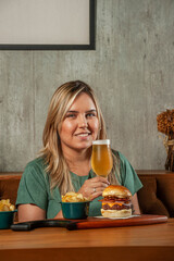 Girl holding a glass of beer with burger sitting at restaurant fast food table - Young people having lunch break at cafe bar