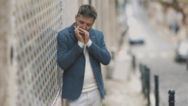 A man stands by a wall on the street and plays the harmonica