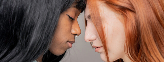 Horizontal banner or header with couple of young lesbian women of different ethnicities head to head while looking down - Caucasian woman and African girlfriend - Lgbtq and gay couple rights concept - obrazy, fototapety, plakaty