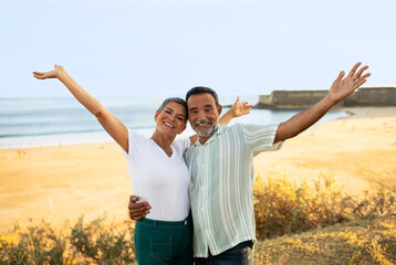 Cheerful Mature Couple Raising Hands Posing Near Ocean Beach Outdoors