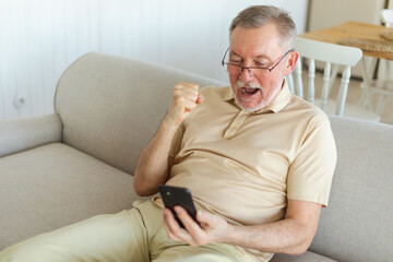 Middle aged senior man euphoric winner with smartphone. Older mature grandfather looking at cell phone reading great news getting good result winning online bid feeling amazed. Winning gesture