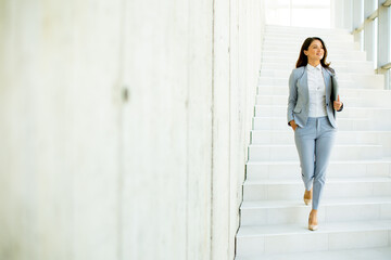 Young business woman walking down the stairs and holding laptop - obrazy, fototapety, plakaty