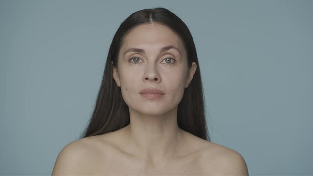 Young seminude woman looks at the camera and smiles tenderly close up on a blue background. Well groomed healthy skin condition. The concept of natural beauty, skin care. HDR BT2020 HLG Material.