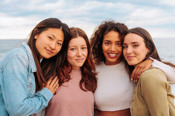 Portrait of four diverse young girl friends standing together on beach.