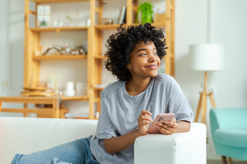 African girl holding smartphone touch screen typing scroll page at home. Woman with cell phone surfing internet using social media apps playing game. Shopping online Internet news cellphone addiction