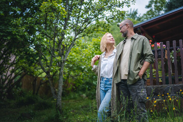 Naklejka na ściany i meble Caucasian happy relaxed middle age couple enjoying summer in country house standing on hugging in garden