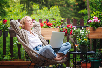 Beautiful happy blonde middle aged woman relaxing on terrace of country house in summer and using...