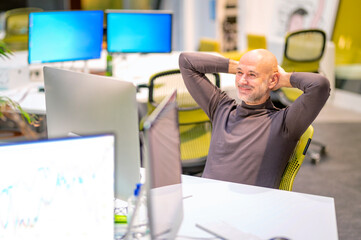 Satisfied businessman sitting at desk and using computers while working in a modern office