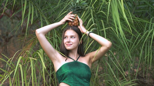 a young woman posing in front of exotic bushes with a pineapple on her head