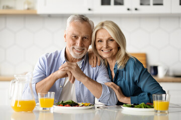 Portrait of happy mature couple posing in kitchen while eating lunch together