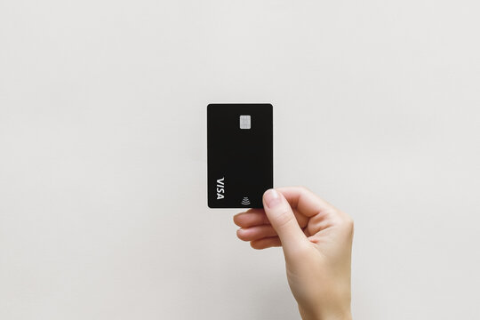 female hand holds a black plastic Visa card on a gray background