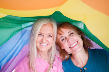 senior couple wrapped with lgtbi flag smiling. Concept: rights, pride, rainbow