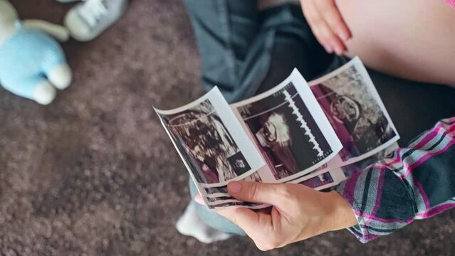 Happy mom stroking her beautiful pregnant belly and looking on ultrasound scan pictures of her baby child, medical examination of baby gender reveal in prenatal period of pregnancy, happiness of