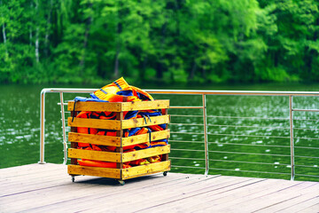 Fototapeta premium Orange life jackets in a wooden box on the pier by the river
