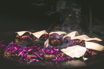 Preparing juicy beef hamburger patties with red cabbage and cheese. BBQ meat sizzling over hot flames. Copy space.