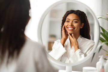 Skincare Concept. Beautiful Young Black Woman Looking In Mirror And Touching Face
