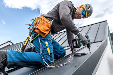 Work at heights. A tinman with a climbing harness and the tool belt on the roof is working with a...