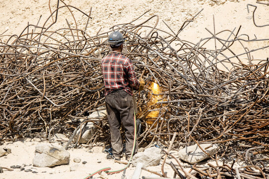 welder is utilizing a welding machine to cut through steel at a bustling construction site. The scorching sun beats down, intensifying the challenging working conditions