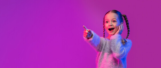 Amazed little girl pointing at copy space, touching face
