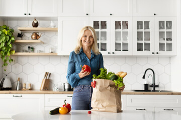 Beautiful Mature Woman Unpacking Paper Bag With Groceries In Kitchen At Home