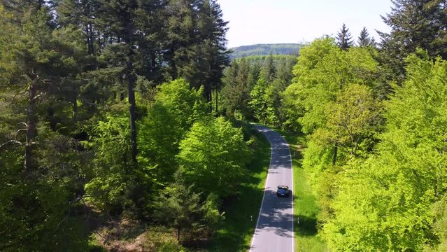 Blue Porsche Boxster Cabrio driving in the German Forest of the Mosel region close to Nurburgring Nordschleife. Cars driving on curvy roads through green woods in the sunny summer day in the hills 
