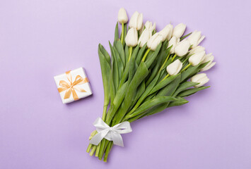 White tulip bouquet with gift on color background, top view