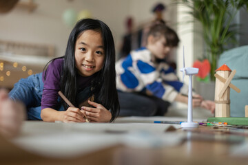 Portrait of a cute Asian girl doing her homework, working on school project about wind energy.