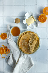 Ingredients for crepes suzette (crepes, orange juice, brown sugar, butter) on white tiled background.