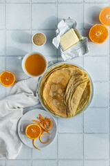 Ingredients for crepes suzette (crepes, orange juice, brown sugar, butter) on white tiled background.