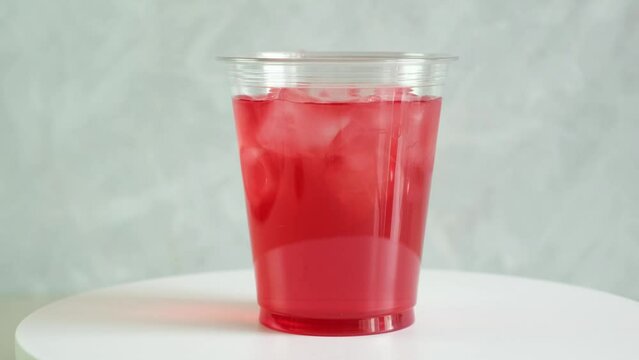 Red iced fruit lemonade or ice tea in take away plastic cup, close-up. Video, 4K, Rotation motion. Refreshing summer drink.