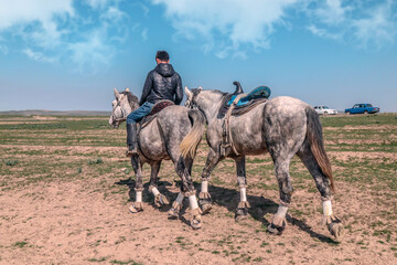 A rider on a horse leading a second black horse in the steppe of Kazakhstan
